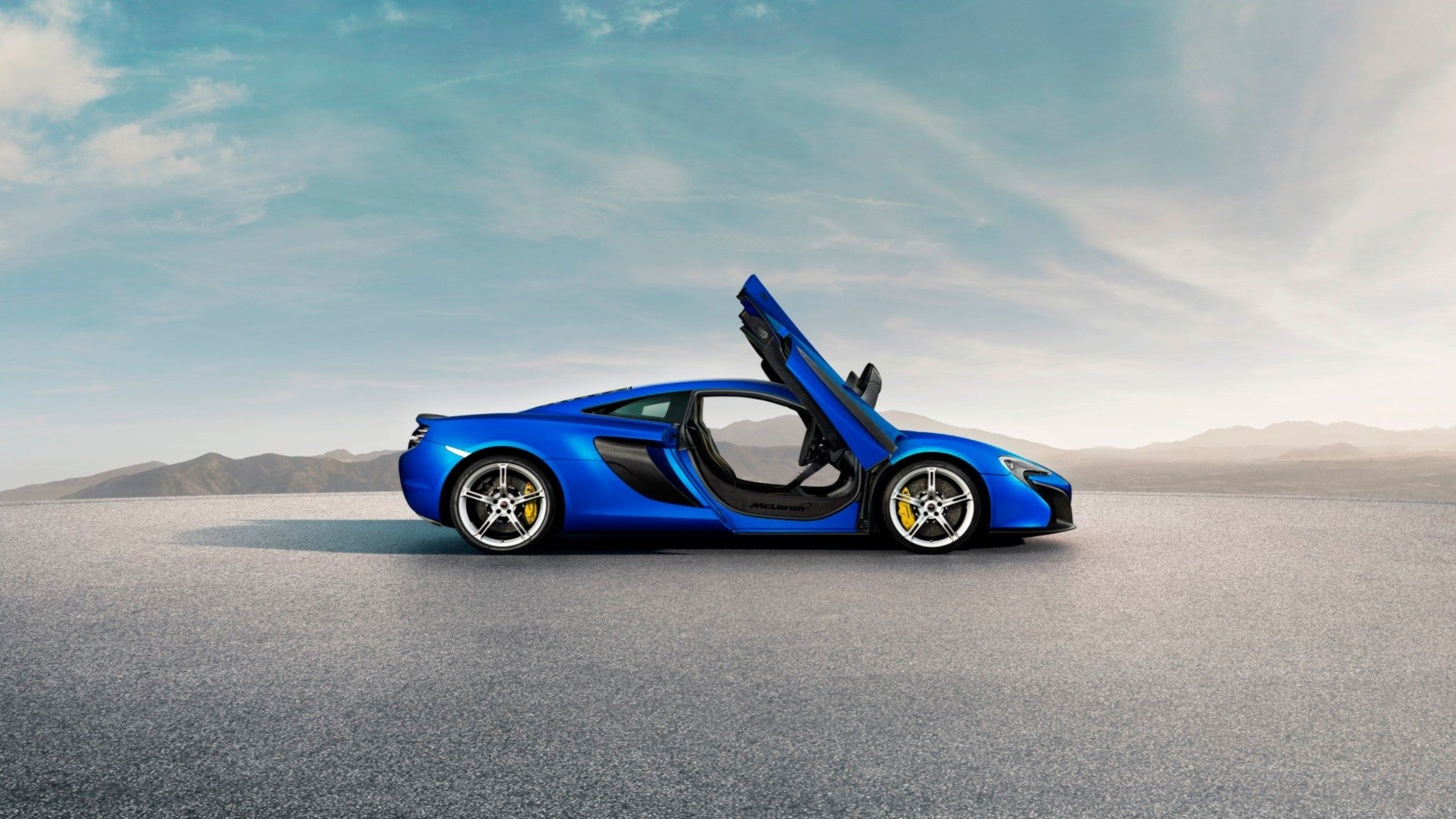 Blue McLaren 650S supercar side profile with dihedral doors open on a wide tarmac beneath a dramatic sky — HD desktop wallpaper background.