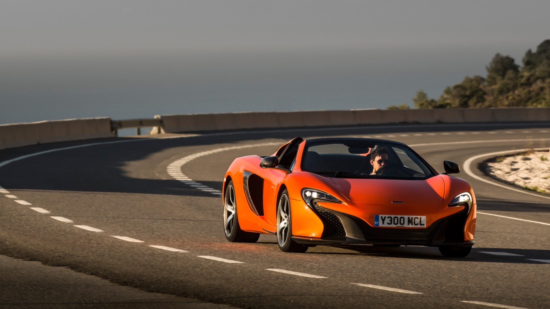 Orange McLaren 650S Spider supercar on a winding coastal road, HD PC desktop wallpaper/background.