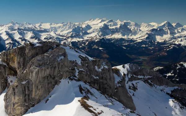 A stunning HD wallpaper showcasing the majestic Alps, featuring snow-capped peaks and rugged rock formations against a clear blue sky, capturing the beauty of nature.