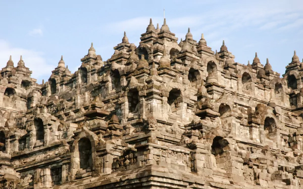 HD PC desktop wallpaper: Borobudur temple close-up showing layered stone stupas and carved reliefs, a religious monument framed by a pale blue sky.