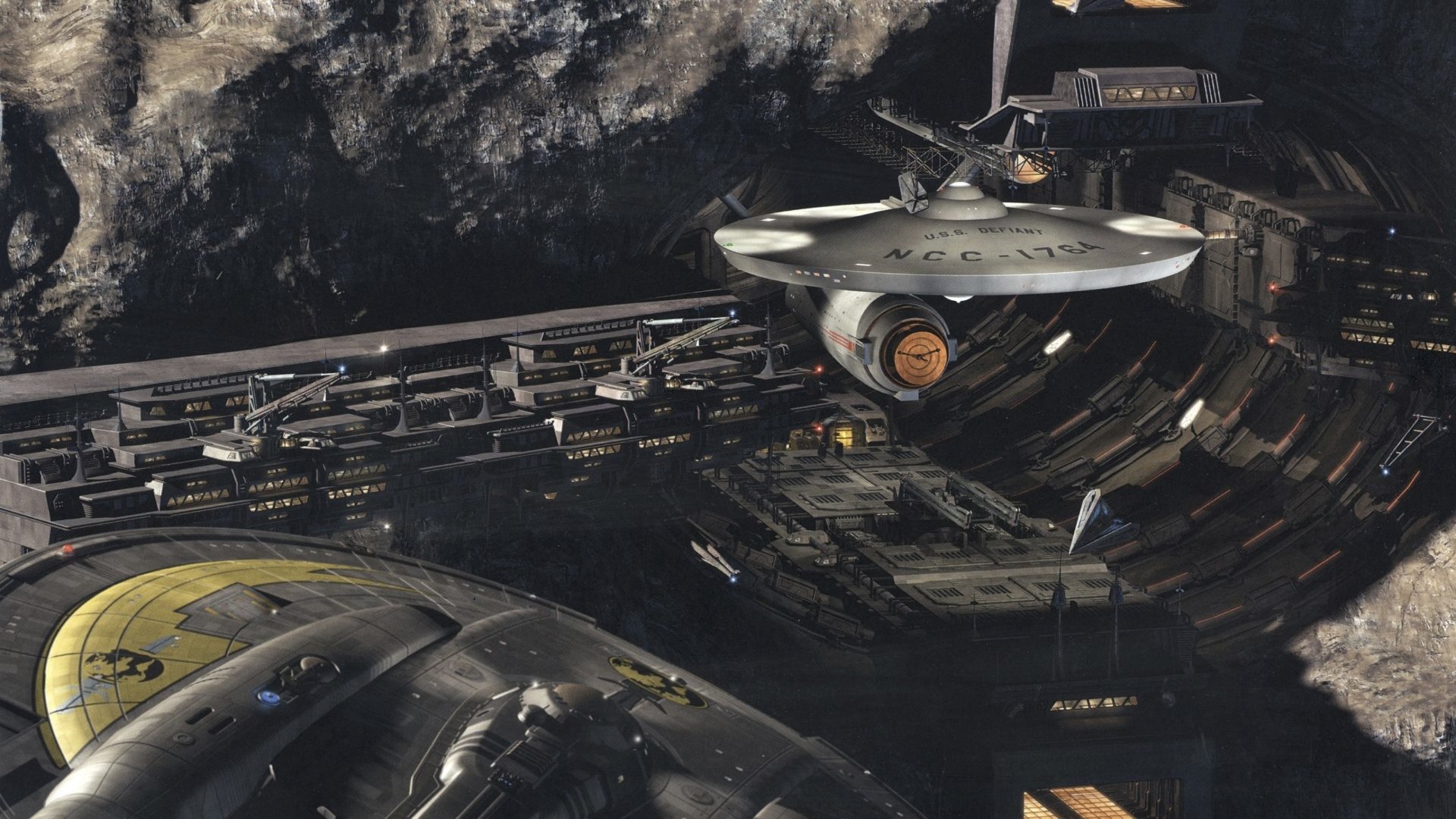 Sci Fi Star Trek 4K Ultra HD PC desktop wallpaper showing a saucer-section starship docked inside a vast orbital shipyard carved into a rocky moon, lit by hangar lights.