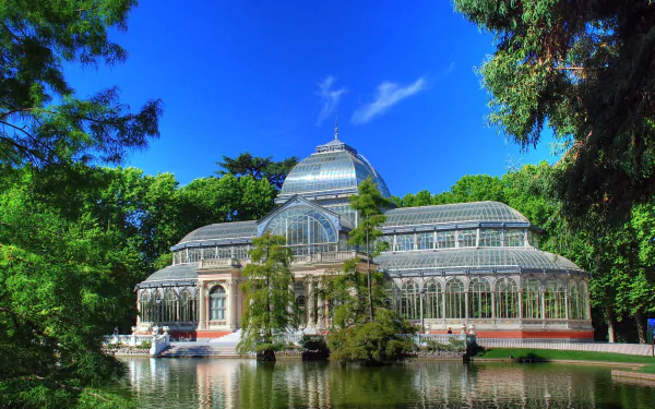 HD desktop wallpaper showcasing the man-made Palacio de Cristal, a stunning glass structure surrounded by lush greenery and reflected in a calm pond.