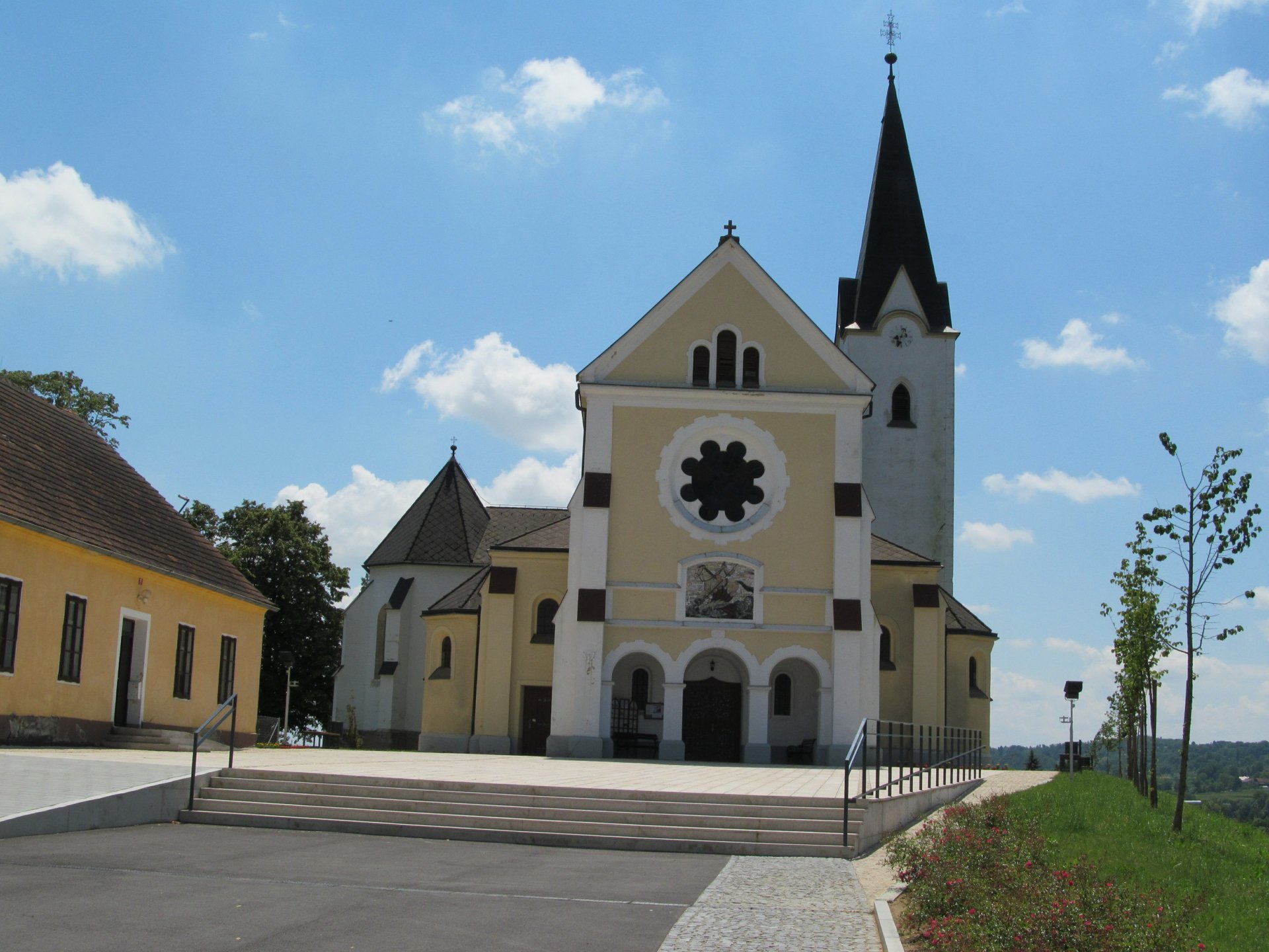 Religious church with tall steeple and rose window on a sunlit plaza under blue sky — 4K Ultra HD PC desktop wallpaper background.