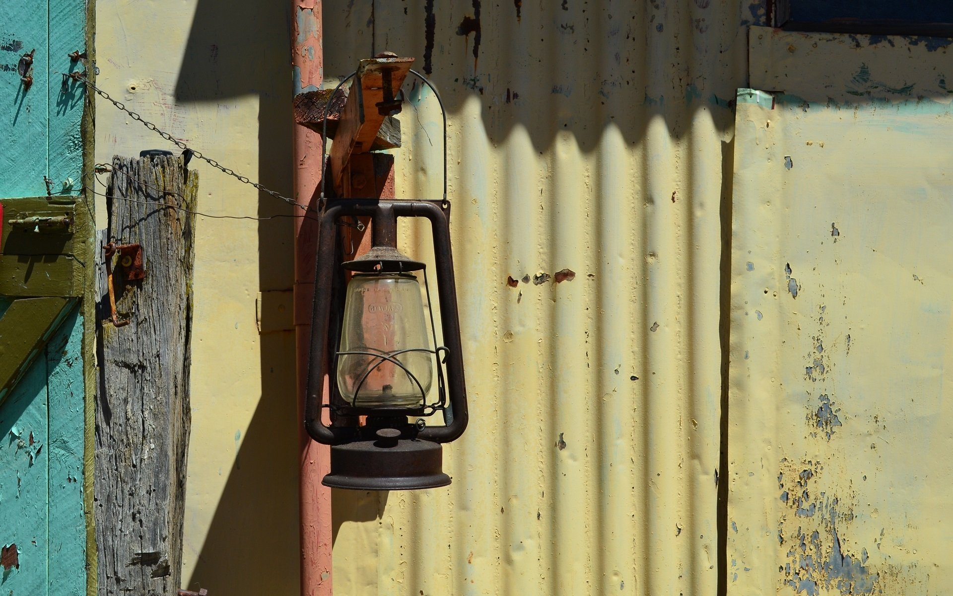 Vintage rusty lantern hanging on a weathered corrugated metal wall, captured in high definition for a PC desktop wallpaper and background.