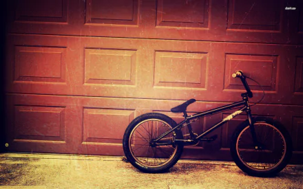 A black bicycle leans against a textured garage door, creating a striking contrast. This HD desktop wallpaper adds a dynamic touch to any screen background.