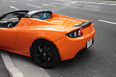 HD desktop wallpaper of an orange Tesla Roadster parked on a city street.