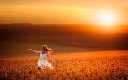 A child in a white dress joyfully spins in a sunlit field at sunset, captured in a vibrant HD photography desktop wallpaper.