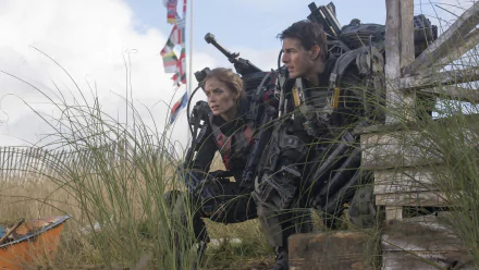 Tom Cruise and Emily Blunt in a tense moment from the movie *Edge of Tomorrow*, crouched behind cover in a combat-ready pose amidst a grassy landscape. 4K Ultra HD wallpaper.