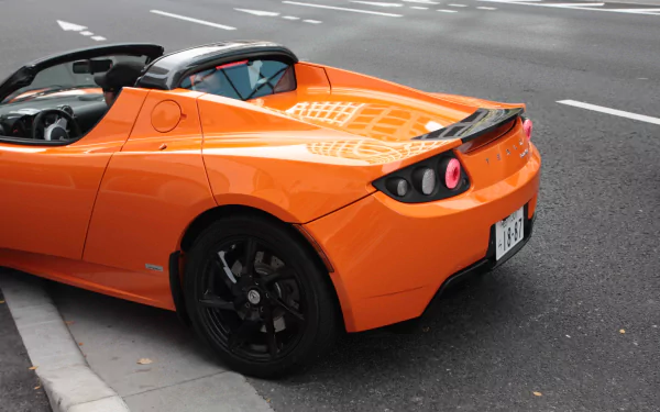 HD desktop wallpaper of an orange Tesla Roadster parked on a city street.