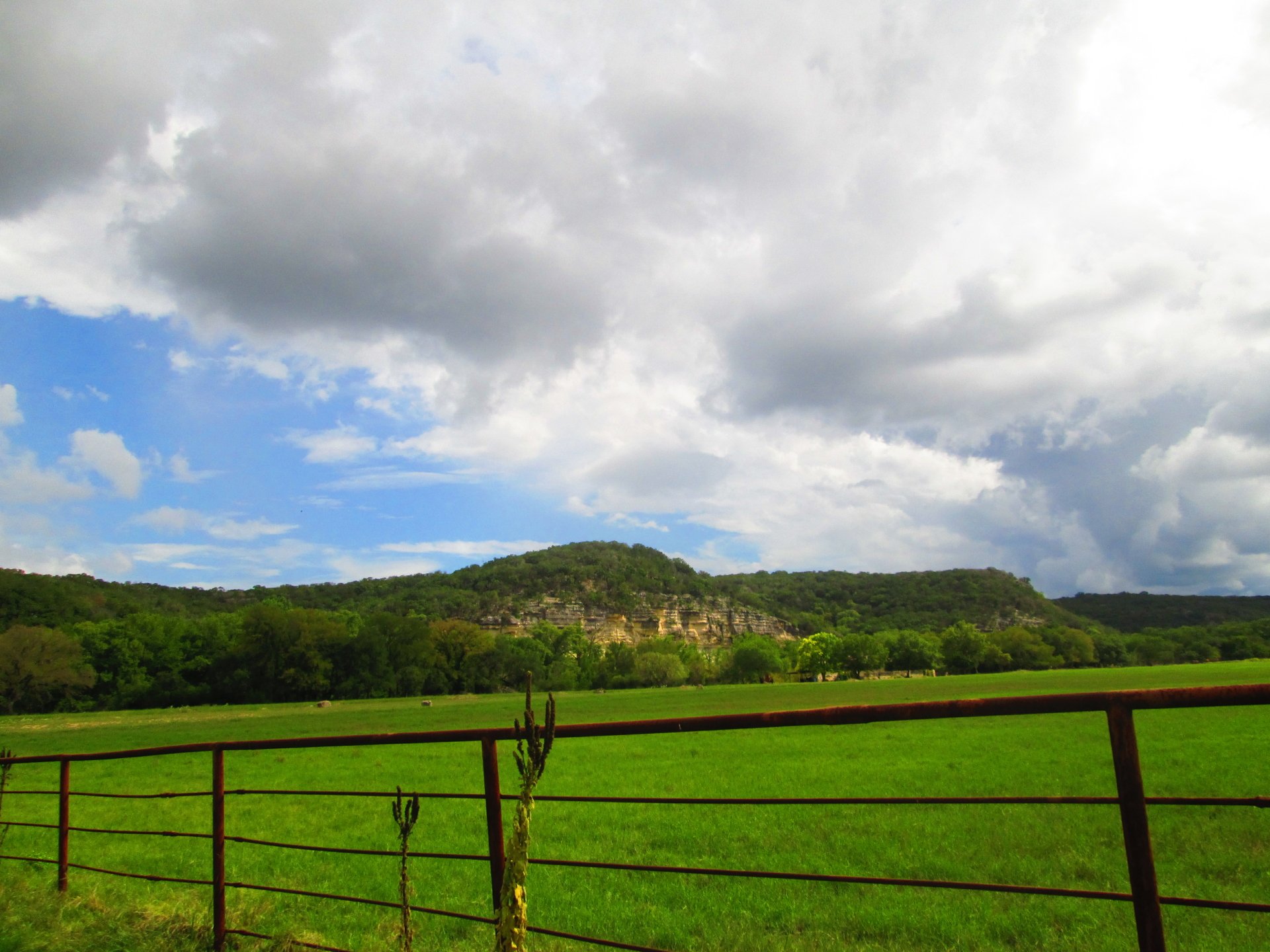 4K Ultra HD PC desktop wallpaper — nature field with a green pasture, metal fence in the foreground, tree-lined hills and a dramatic cloudy sky.