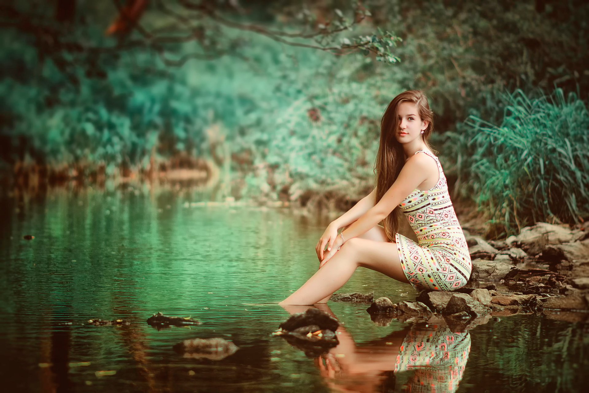 HD desktop wallpaper featuring a serene woman sitting by a tranquil forest pond, reflecting a contemplative mood.