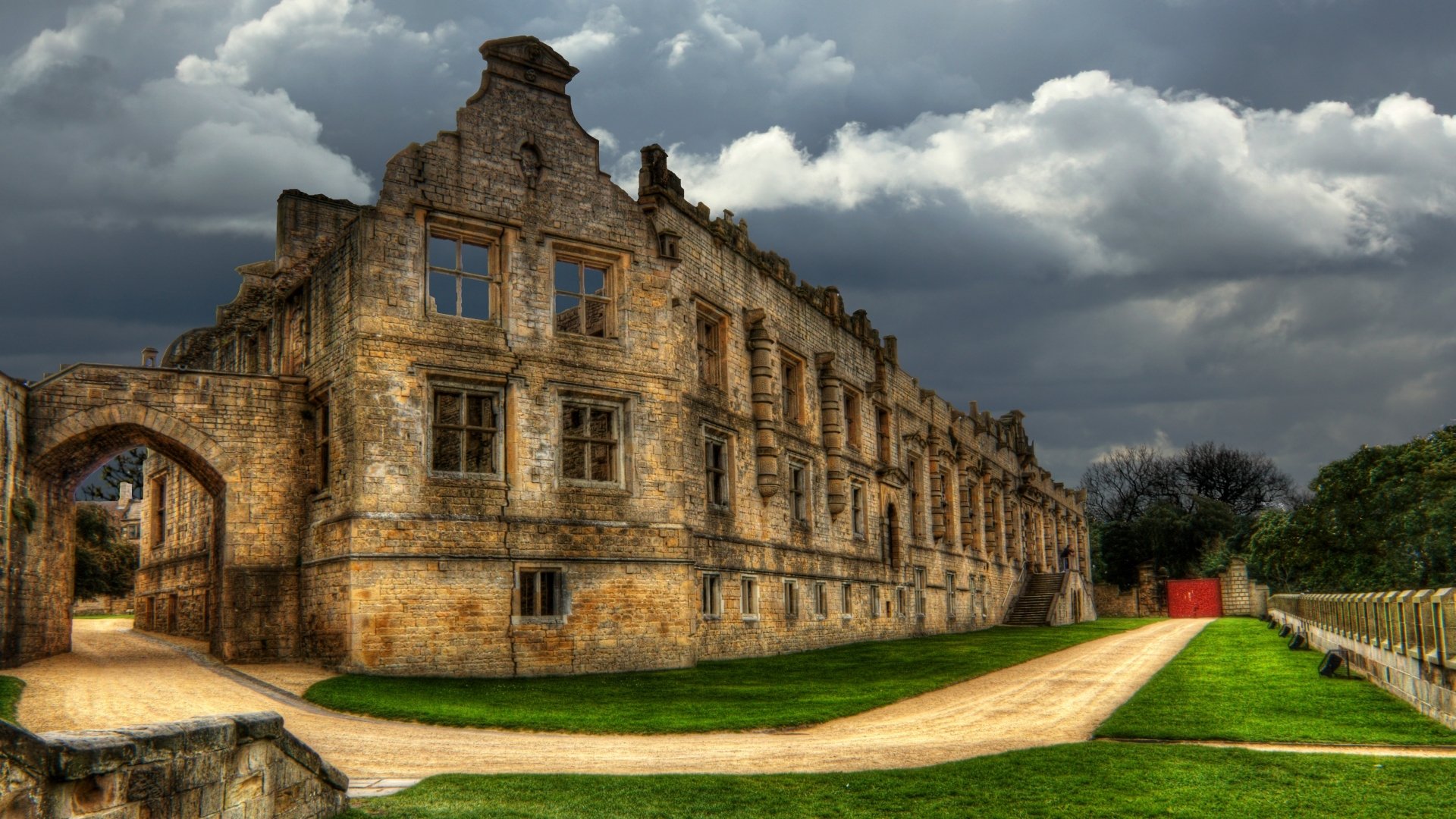 HD PC desktop wallpaper and background of Bolsover Castle, a man-made stone facade under dramatic clouds, green lawns and a winding path beside the ruined building.