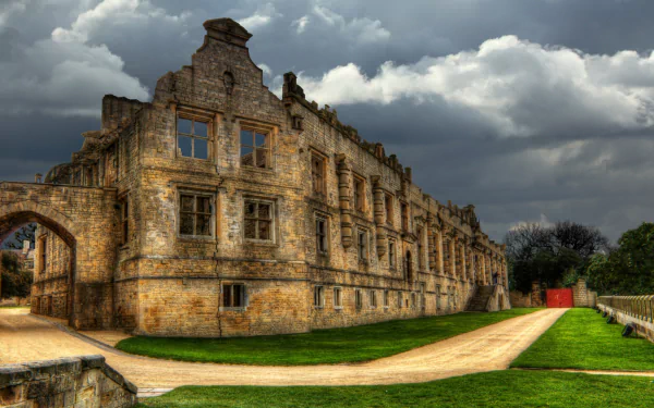 HD PC desktop wallpaper and background of Bolsover Castle, a man-made stone facade under dramatic clouds, green lawns and a winding path beside the ruined building.