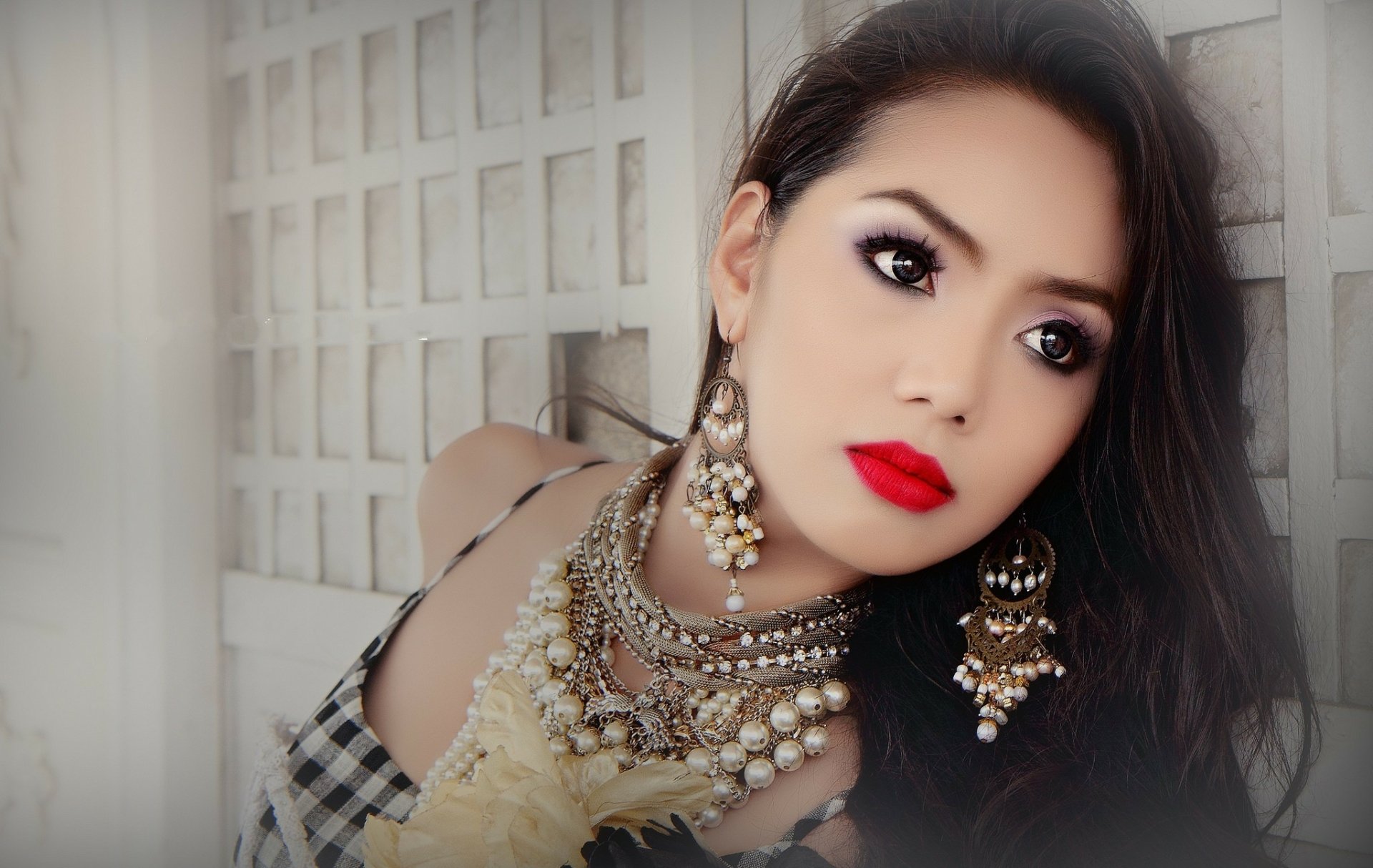 An HD desktop wallpaper featuring a woman with red lipstick and elaborate jewelry against a lattice backdrop.