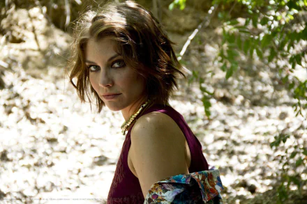 A striking HD desktop wallpaper featuring Lauren Cohan, set in a natural environment, showcasing her captivating gaze amidst a backdrop of dappled light and greenery.