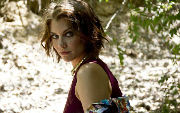 A striking HD desktop wallpaper featuring Lauren Cohan, set in a natural environment, showcasing her captivating gaze amidst a backdrop of dappled light and greenery.