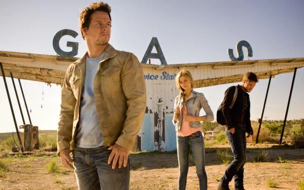 A scene from Transformers: Age of Extinction featuring three characters in front of an abandoned gas station, conveying a sense of adventure in a post-apocalyptic landscape.