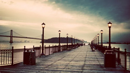 Sunset view of Pier 7 in San Francisco, showcasing the Bay Bridge in the background. The wooden pier is lined with lamps, creating a tranquil atmosphere over the water.