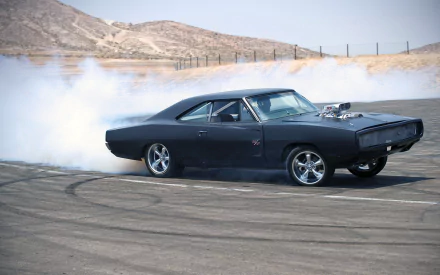 A sleek black Dodge Charger R/T drifts on a dusty track, with tires smoking against a backdrop of rolling hills, showcasing its powerful stance and dynamic performance. HD desktop wallpaper.
