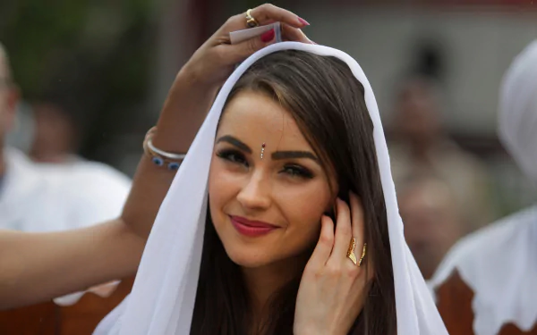 American celebrity and model Olivia Culpo smiles gently, adjusting a white headscarf in this HD PC desktop wallpaper and background image.