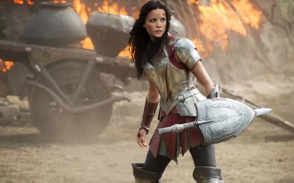 HD PC desktop wallpaper featuring a fierce warrior woman from the movie Thor: The Dark World, clad in armor and holding a large sword amidst a fiery battlefield.