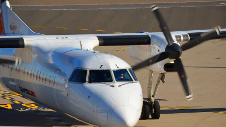 A close-up view of a QantasLink Bombardier Dash 8 Q315 aircraft on the tarmac, showcasing its twin propellers and sleek design in high definition.