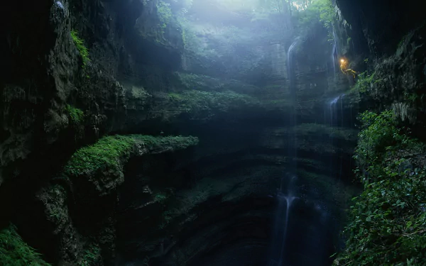 A serene cave landscape bathed in soft light, with lush greenery and cascading water, capturing the tranquil beauty of nature. HD wallpaper for an immersive desktop experience.