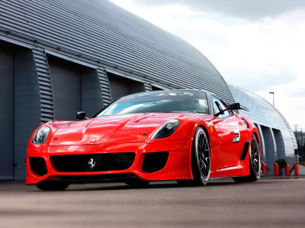 HD PC desktop wallpaper of a red Ferrari vehicle — a 2009 Ferrari 599XX shown low-angle in front of a modern hangar, highlighting its aggressive front end and aerodynamic details.