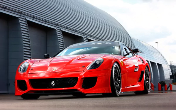 HD PC desktop wallpaper of a red Ferrari vehicle — a 2009 Ferrari 599XX shown low-angle in front of a modern hangar, highlighting its aggressive front end and aerodynamic details.