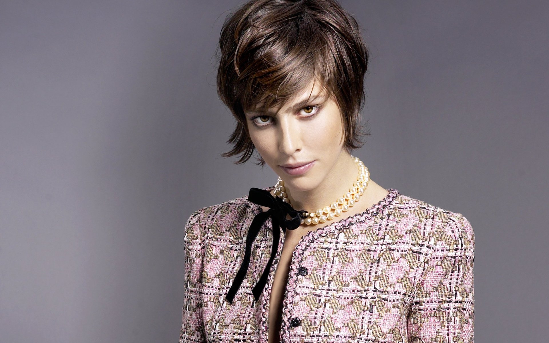 HD desktop wallpaper: portrait of a short-haired actress in a pink tweed jacket and pearl necklace, posed against a soft gray background.