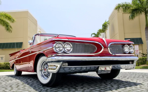 HD PC desktop wallpaper showing a red Pontiac Bonneville vehicle from a low angle, parked on a sunlit cobblestone courtyard with palm trees and modern buildings.