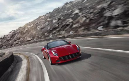 Red Ferrari California T vehicle speeding on a winding coastal mountain road, captured as a dynamic 2K Quad HD PC desktop wallpaper background.
