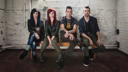 A HD desktop wallpaper featuring the band Skillet, showcasing four members seated against a rustic background, dressed in stylish, casual attire with an edgy vibe.