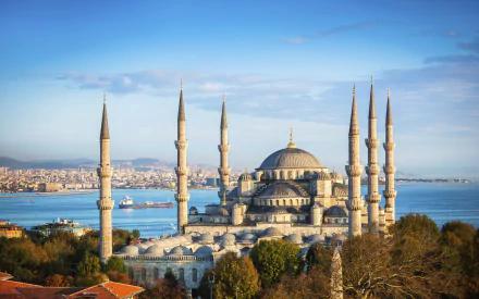 A stunning HD image of the Sultan Ahmed Mosque, showcasing its majestic domes and towering minarets against a scenic backdrop of the city and water.
