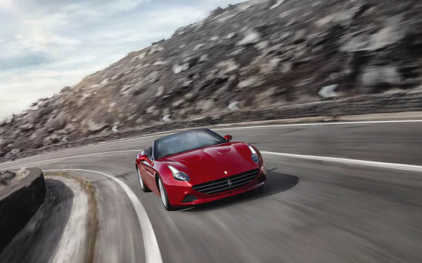 Red Ferrari California T vehicle speeding on a winding coastal mountain road, captured as a dynamic 2K Quad HD PC desktop wallpaper background.