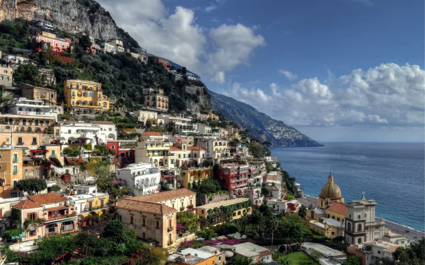 Scenic view of Positano, Salerno, Italy, showcasing colorful hillside buildings overlooking the Mediterranean Sea under a partly cloudy sky.
