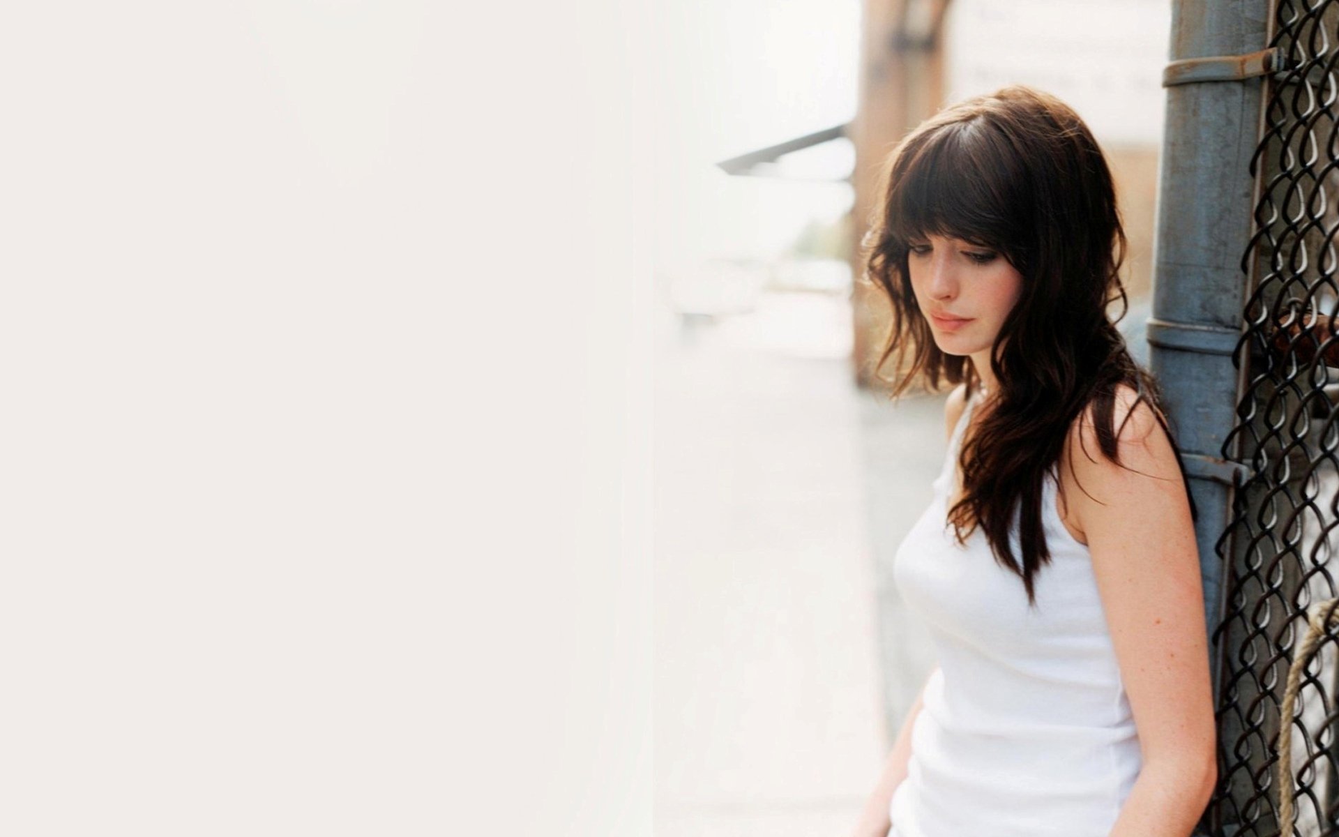 A serene HD wallpaper featuring Anne Hathaway, showcasing her in a white top against an urban backdrop, exuding elegance and introspection.