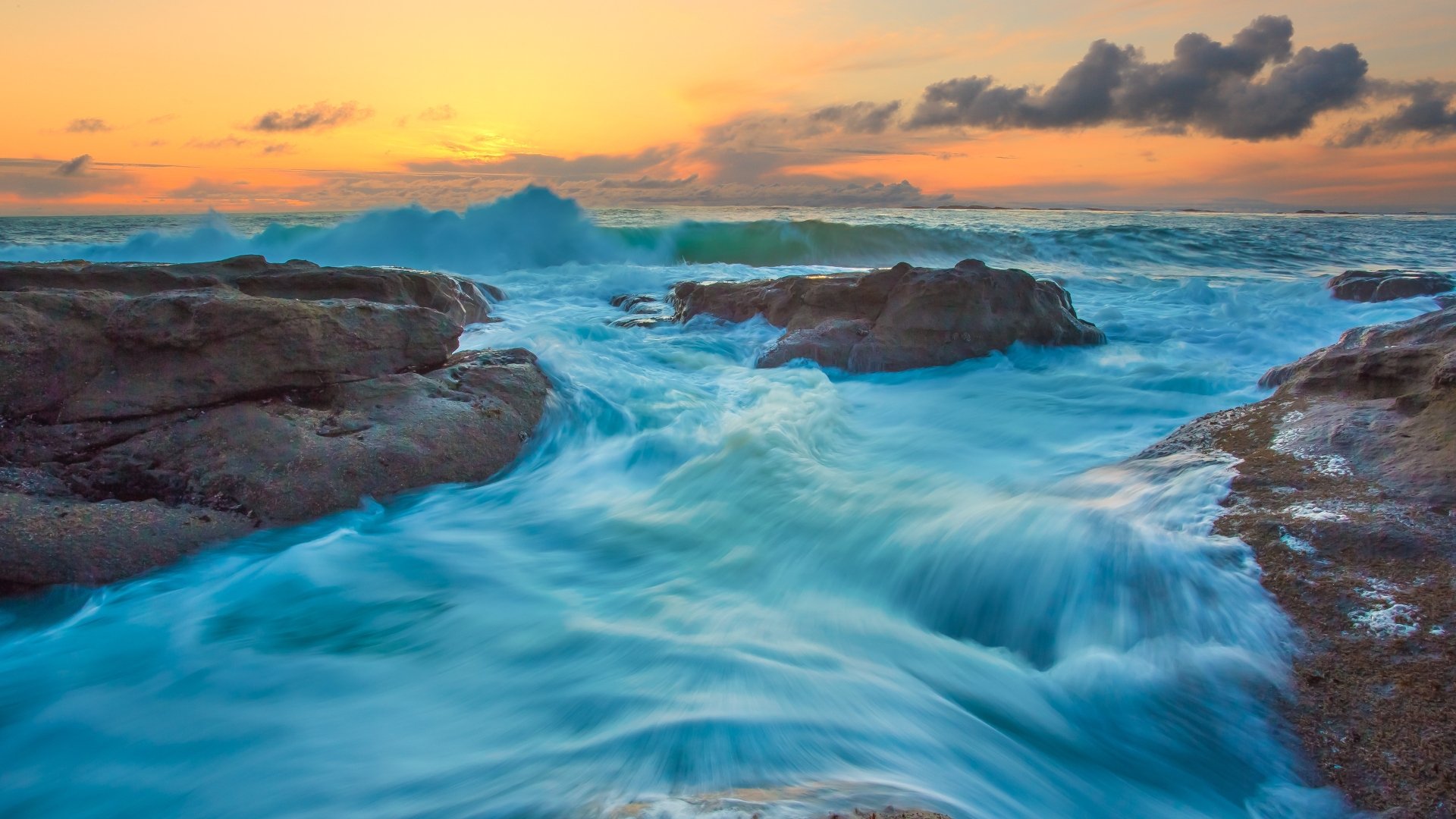 4K Ultra HD ocean waves crash against rocky shores under a vibrant sunset sky, capturing the dynamic beauty of nature.