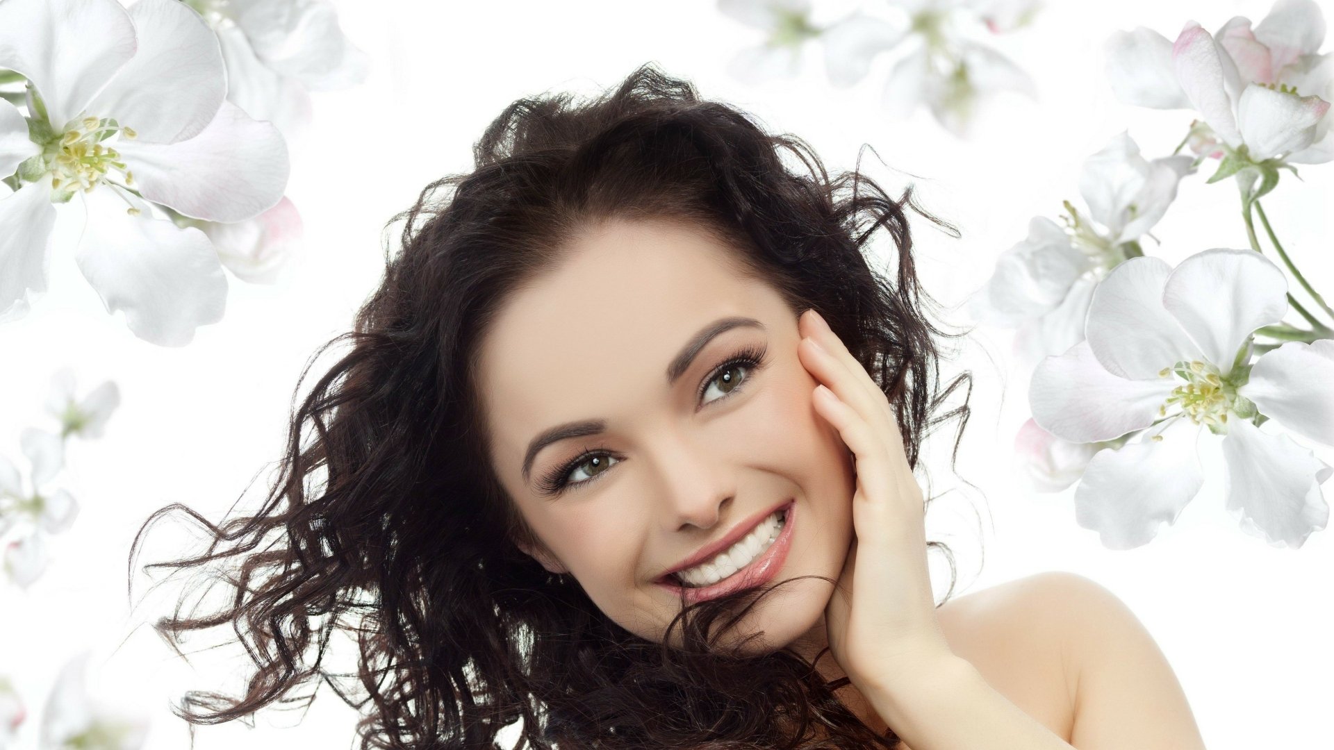 HD desktop wallpaper featuring a smiling woman with curly hair, set against a backdrop of blooming white flowers.