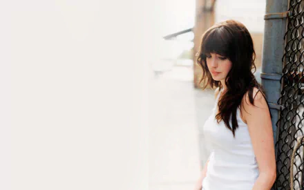 A serene HD wallpaper featuring Anne Hathaway, showcasing her in a white top against an urban backdrop, exuding elegance and introspection.
