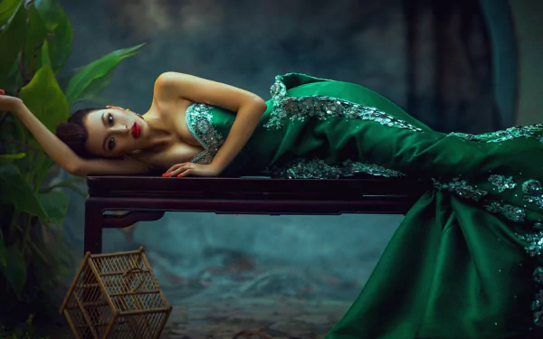 Asian woman in an elegant green dress reclining on a dark wooden surface, featured in an HD PC desktop wallpaper and background.