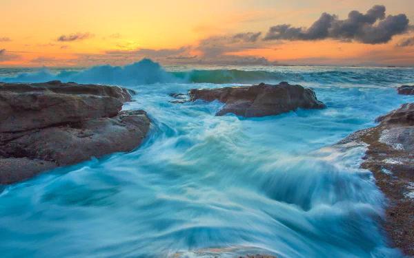 4K Ultra HD ocean waves crash against rocky shores under a vibrant sunset sky, capturing the dynamic beauty of nature.