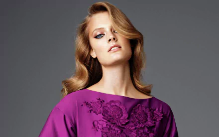 HD PC desktop wallpaper: French fashion model woman with blonde waves in a purple embroidered top, posed against a neutral gray background.