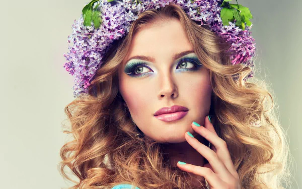A woman with flowing curls adorned in a lilac wreath gazes thoughtfully, showcasing a fresh makeup look. This vibrant image serves as an eye-catching HD desktop wallpaper.