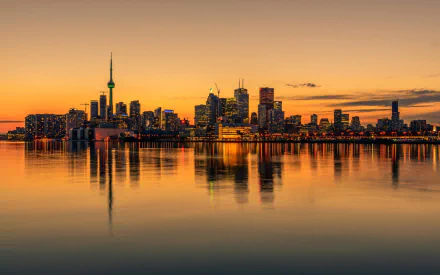 A stunning HD desktop wallpaper of Toronto's skyline at sunset, reflecting on calm waters, showcasing the city's iconic architecture and vibrant atmosphere.