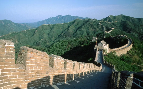 A stunning HD desktop wallpaper featuring the Great Wall of China, showcasing its impressive structure winding through lush green mountains under a clear blue sky.