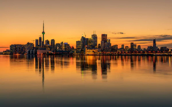 A stunning HD desktop wallpaper of Toronto's skyline at sunset, reflecting on calm waters, showcasing the city's iconic architecture and vibrant atmosphere.