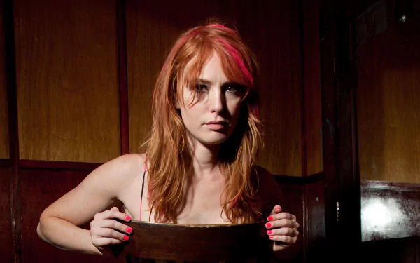 HD desktop wallpaper featuring American actress Alicia Witt with red hair against a dark wooden background, captured in a moody, intimate portrait style.