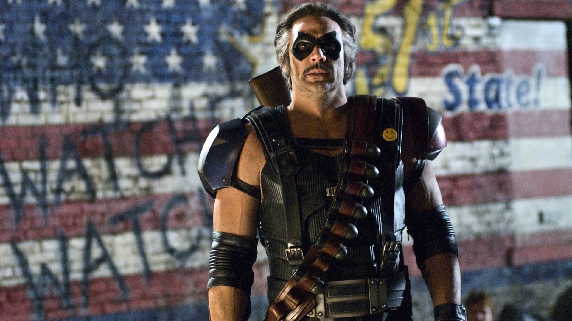 HD PC desktop wallpaper from the Watchmen movie: a masked, armored vigilante wearing a bandolier stands before a weathered American flag, exuding gritty urban heroism.