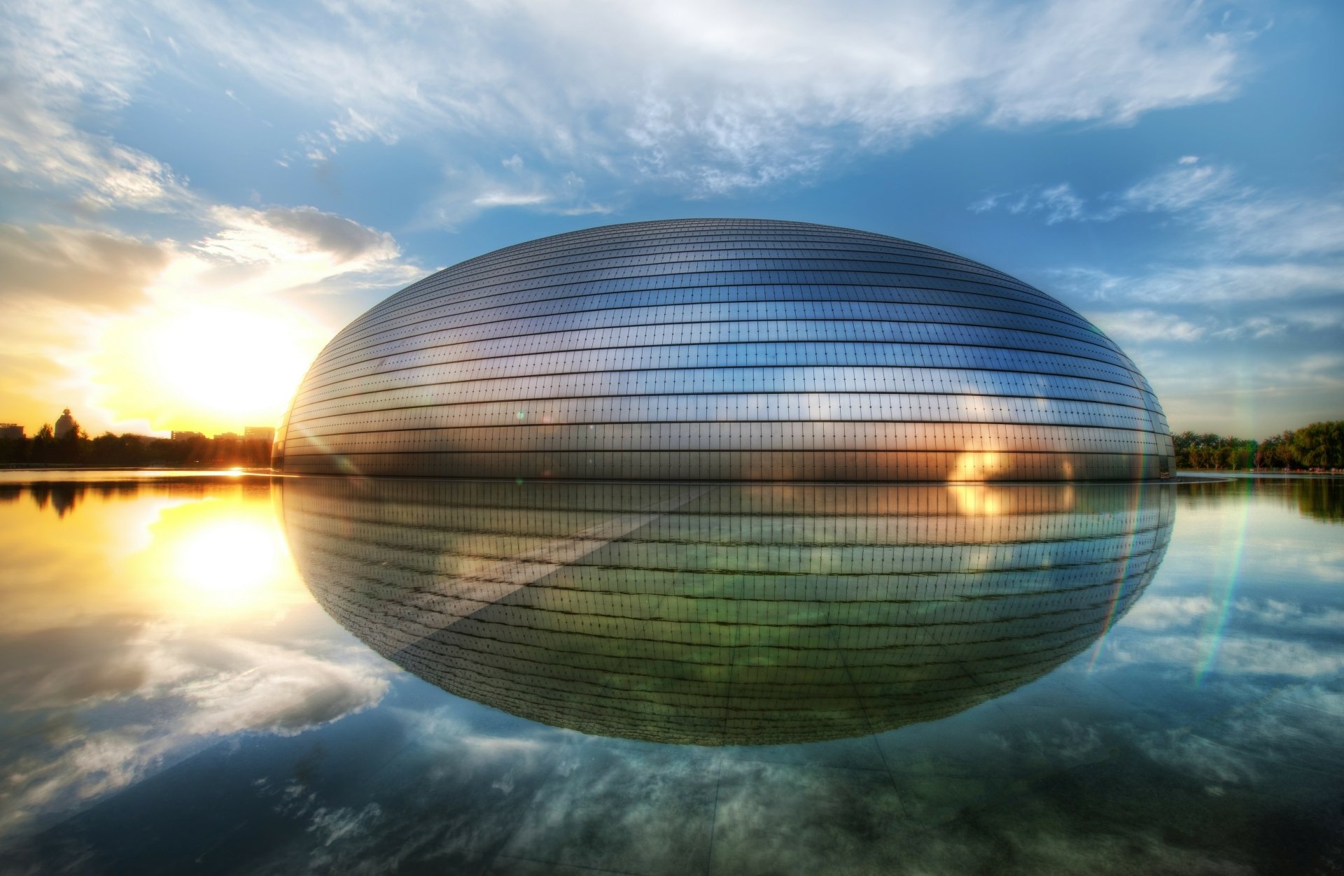 The Beijing National Grand Theatre in China reflects on calm water at sunset, showcasing its sleek, modern architecture in this 4K Ultra HD landscape wallpaper.